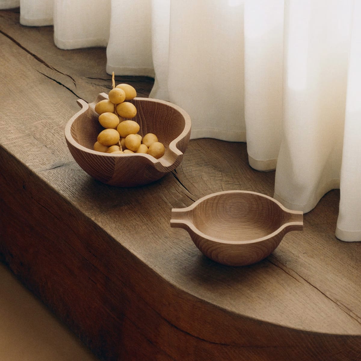 Two Georg Jensen Koppel bowls made of oak nested together on a minimalist table.
